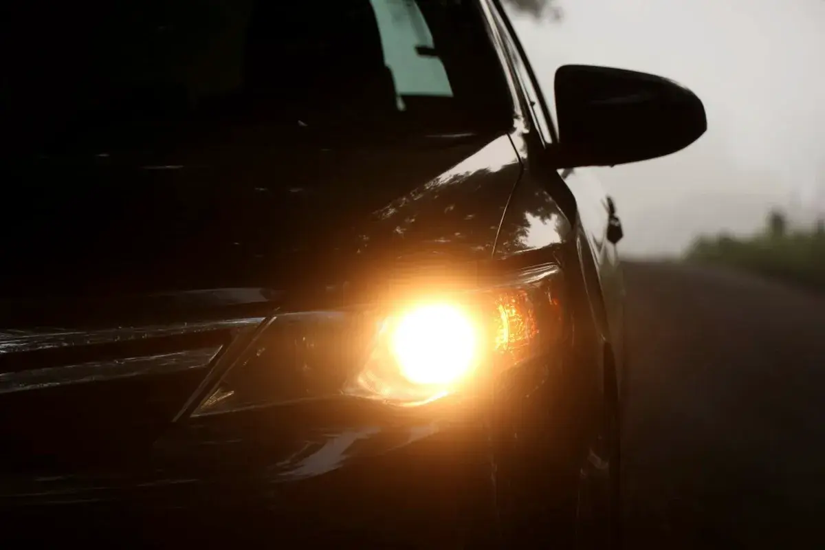 Luz amarela acesa na frente de um carro preto em dia de neblina. Imagem ilustrativa.