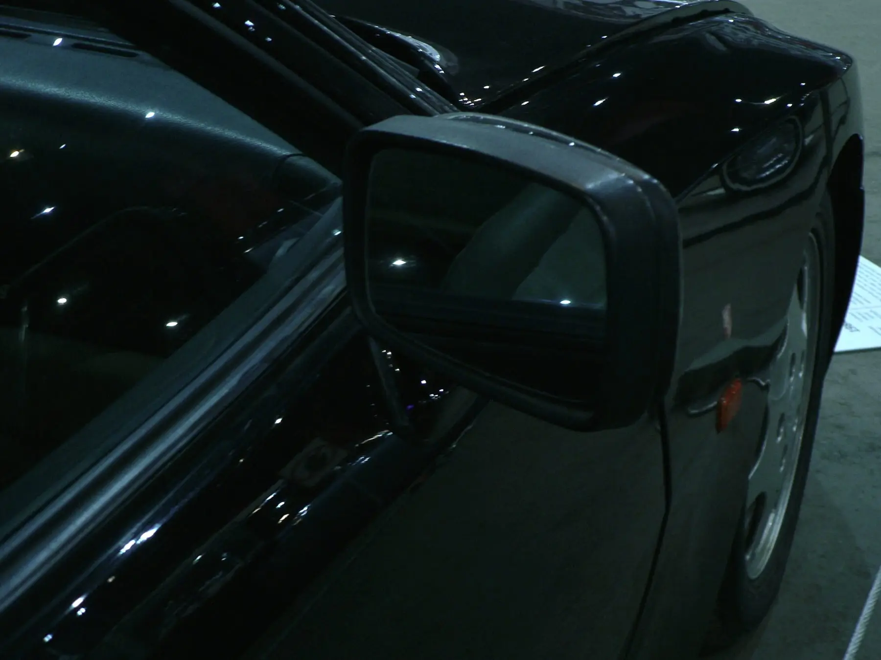 Retrovisor e lateral de um carro preto com reflexos suaves da luz. Imagem ilustrativa.